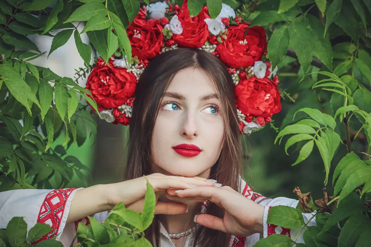 Дівчина у вінку з червоних троянд і вишитій сорочці серед зелені