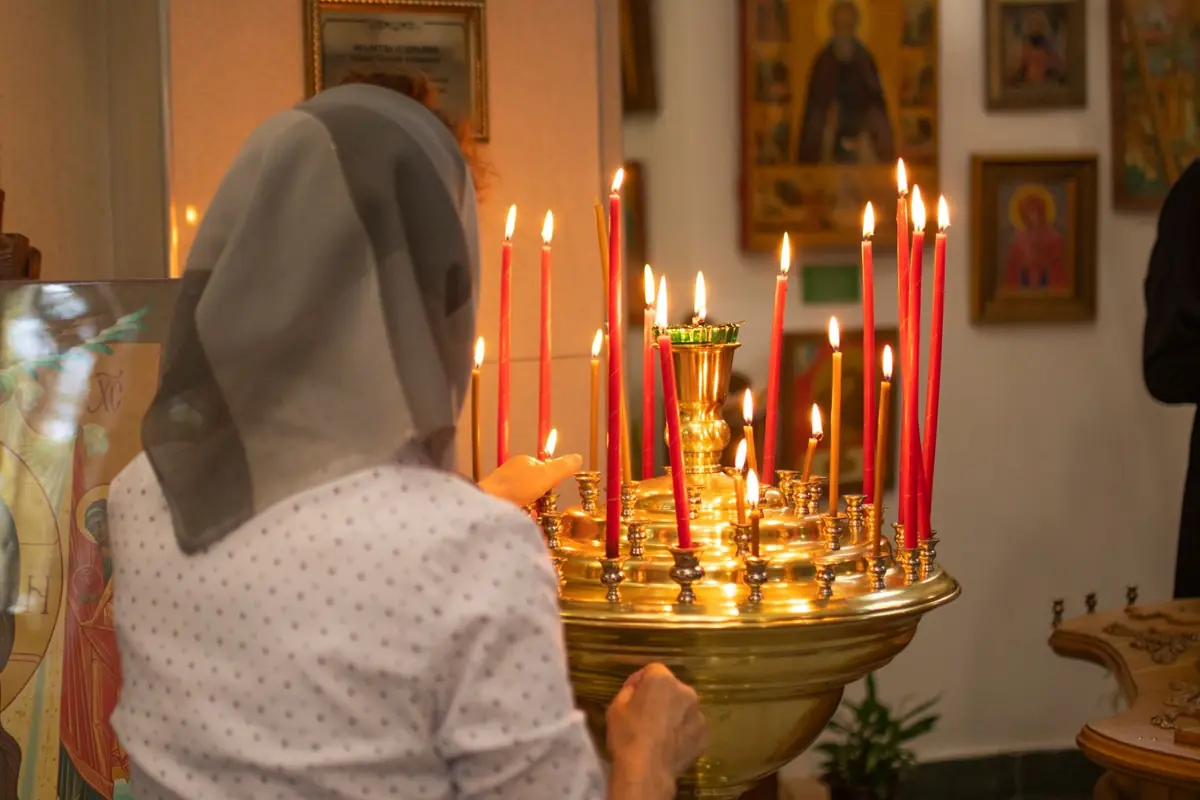 Жінка в хустці ставить свічку біля свічника в храмі з іконами